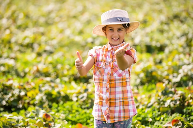 gelukkig jong kindmeisje dat aardbeien plukt en eet op een plantage