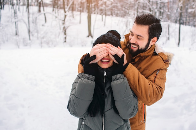 Gelukkig jong koppel in de winter. Familie buitenshuis. man en vrouw naar boven kijken en lachen. Liefde, plezier, seizoen en mensen - wandelen in winterpark. Hij bedekte haar ogen met haar handen