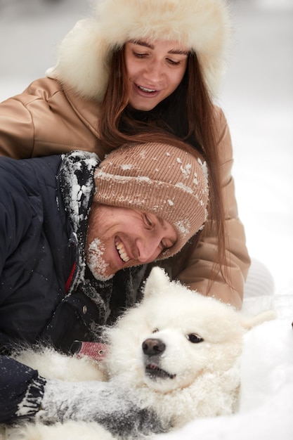 Gelukkig jong koppel in winterwear spelen met raszuivere siberische husky en plezier in ingesneeuwd dennenbos