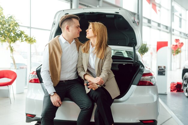 Gelukkig jong koppel kiest en koopt een nieuwe auto voor het gezin in de dealer.