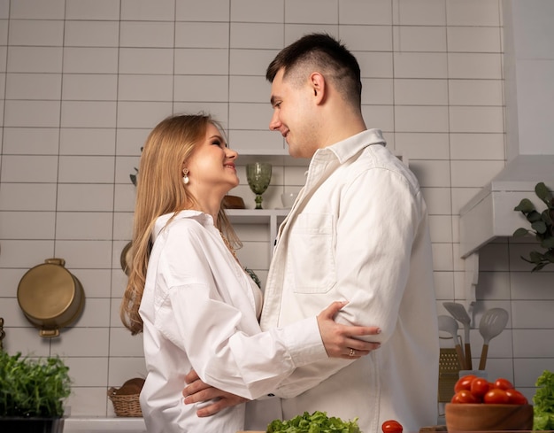 Gelukkig jong koppel knuffelen tijdens het koken thuis knappe man en mooie vrouw kijken naar elkaar