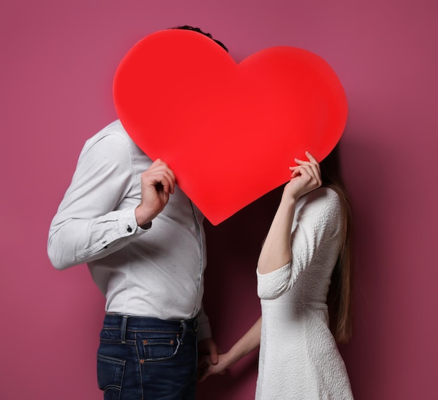 Gelukkig jong koppel met rood papier hart op kleur achtergrond