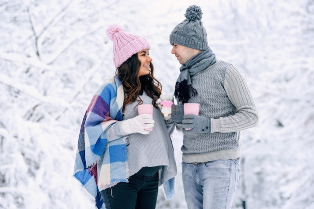 Gelukkig jong koppel wandelen in een besneeuwd park met roze kopjes thee en roze koekjes