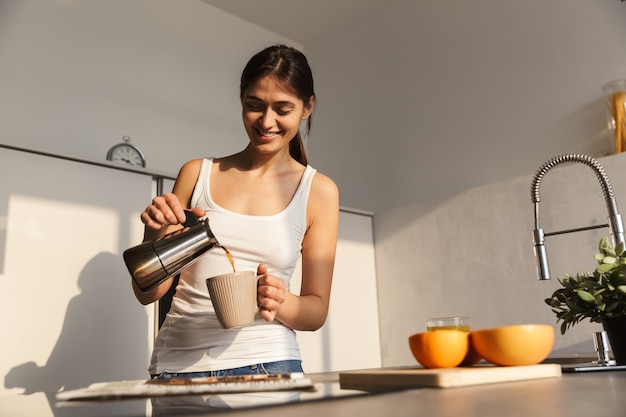 Gelukkig jong meisje dat 's ochtends bij de keuken staat, met een kopje koffie