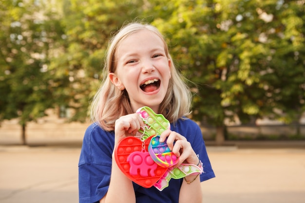 Gelukkig jong meisje dat vrolijk schreeuwt en veel pop-it-speelgoed vasthoudt