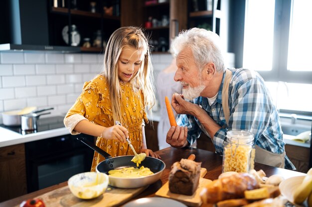 Gelukkig jong meisje en haar grootvader koken samen in de keuken