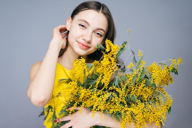 Gelukkig jong meisje geniet van de warmte houdt in haar handen een geurige gele mimosa