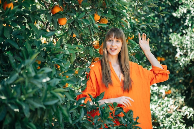 Gelukkig jong meisje in oranje jurk poseert voor de camera door haar handen op te houden in de oranje tuin