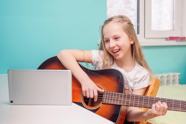 Foto gelukkig jong meisje leert gitaar spelen de gitarist kijkt naar de tablet