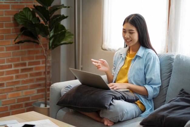 Gelukkig jong meisje met videogesprek op laptop terwijl ze thuis op de bank zit