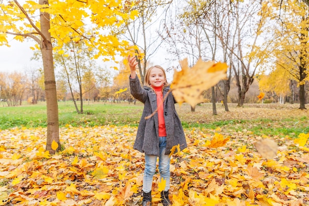 Gelukkig jong meisje spelen onder vallende gele bladeren in prachtig herfstpark op natuurwandelingen buiten. klein kind werpt herfst oranje esdoorn bladeren.