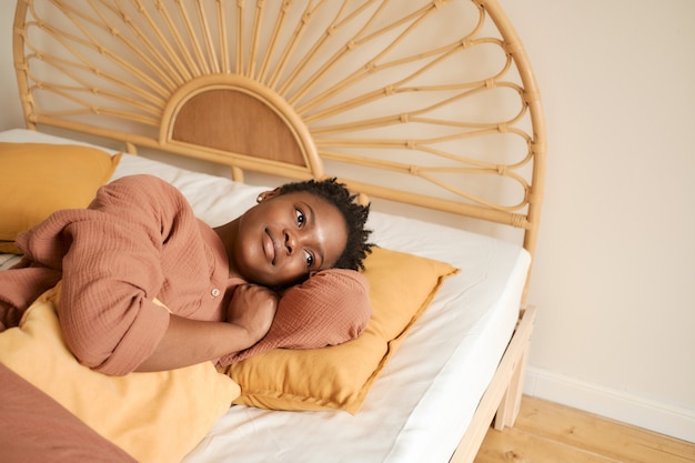 Gelukkig jong meisje zittend op bed in de slaapkamer en met behulp van laptop mousseline pyjama chatten met vrienden