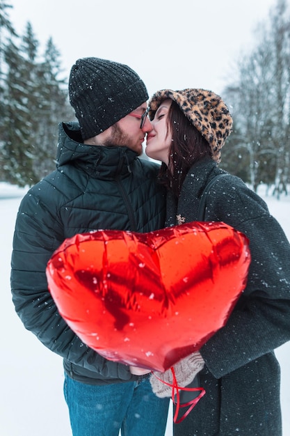 Gelukkig jong mooi paar geliefden een man en een vrouw in modieuze winterkleding met een rode heide ballon en kussen in een park met sneeuw