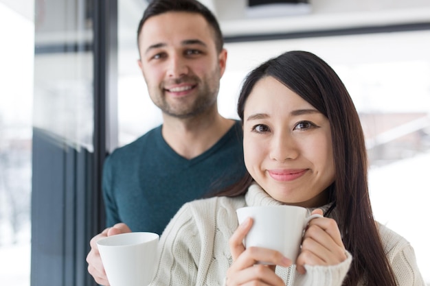 gelukkig jong multi-etnisch paar genietend van koffie in de ochtend bij het raam op koude winterdag thuis