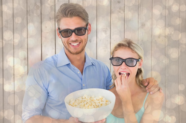 Gelukkig jong paar die 3d glazen dragen die popcorn eten tegen het licht gloeiende patroon van het puntenontwerp