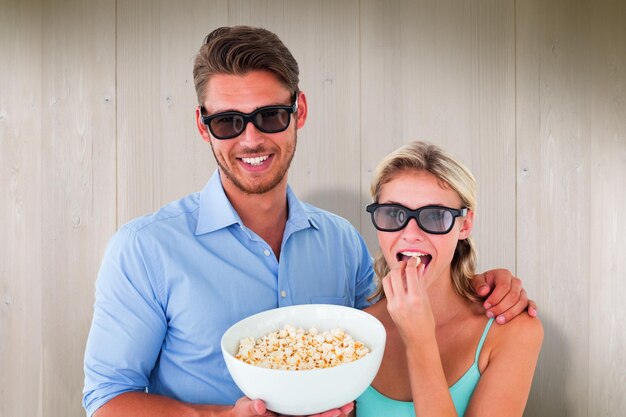 Foto gelukkig jong paar die 3d glazen dragen die popcorn eten tegen houten planken