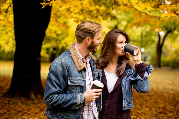 Gelukkig jong paar met koffiekoppen die in de herfstpark lopen