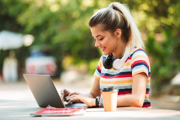 Foto gelukkig jong schattig meisje student zitten in park met behulp van laptopcomputer.