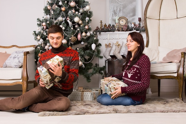 Gelukkig jong stel dat Kerstmis viert, zittend op een tapijt voor de kerstboom en geschenken uitwisselt