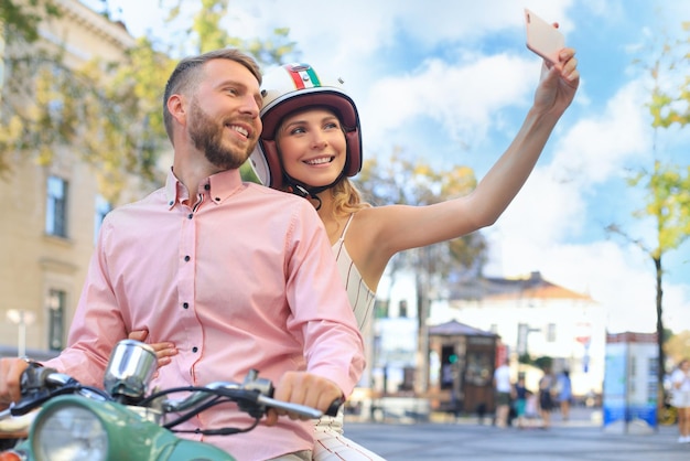 Gelukkig jong stel dat selfie op smartphone neemt terwijl ze buiten op scooter zitten