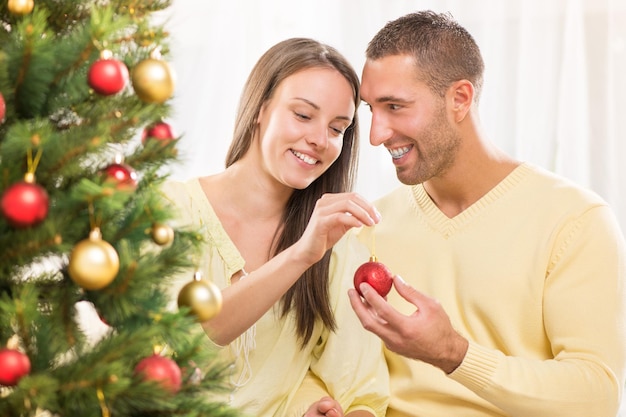 Gelukkig jong stel geniet van het versieren van de kerstboom thuis.