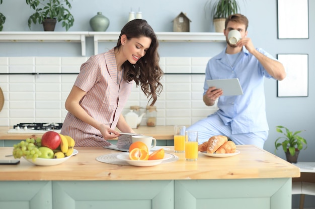 Gelukkig jong stel in pyjama kijken naar online inhoud in een didital-tablet en lachend in de keuken thuis.