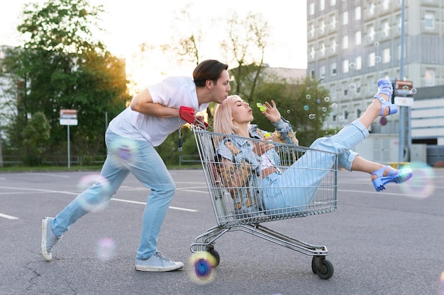 Gelukkig jong stel veel plezier met een winkelwagentje en bellen blazen op de parkeerplaats van een supermarkt