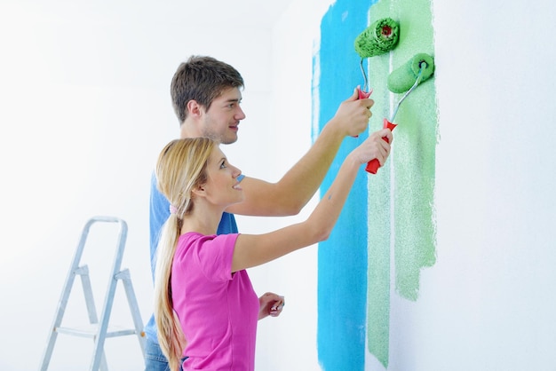 Foto gelukkig jong stel verf in groene en blauwe kleur witte muur van hun nieuwe huis