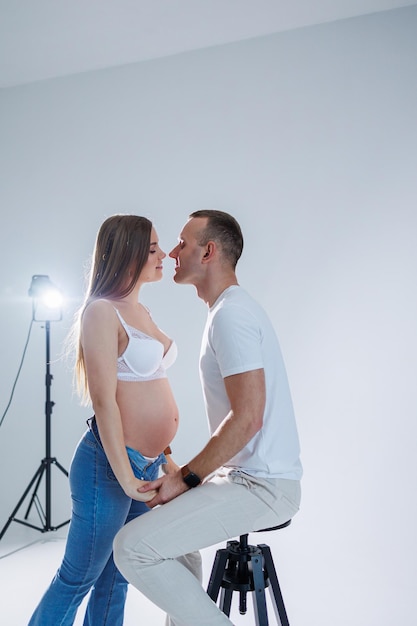 Gelukkig jong stel verwacht een baby in witte t-shirts en spijkerbroeken op een witte achtergrond geluk van zwangerschap en bevalling Een gelukkig getrouwd stel verwacht een kind