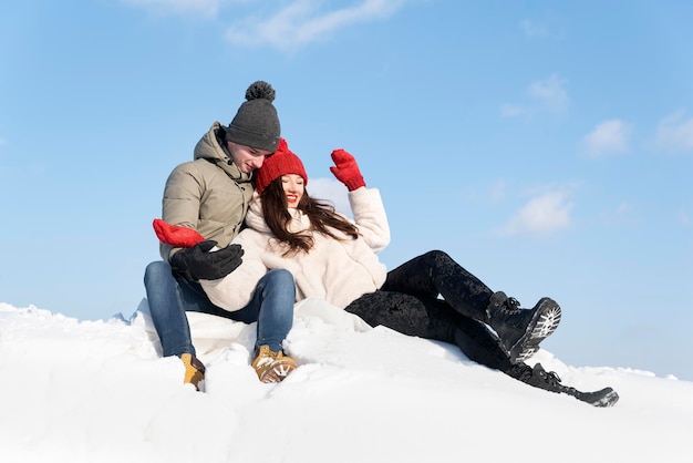 Gelukkig jong stel zit bovenop een besneeuwde heuvel, kerel knuffelt zijn vriendin Paar verliefd op zonnige winterdag