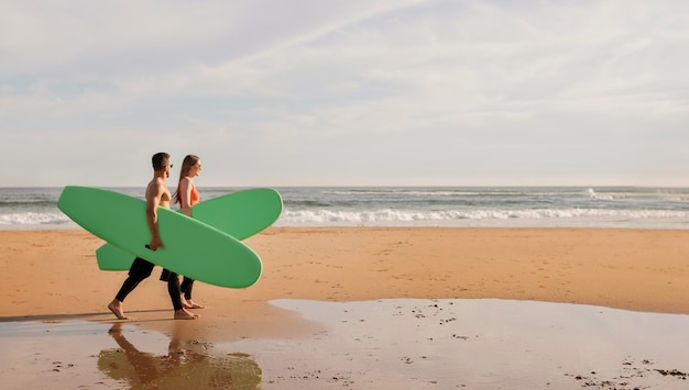 Gelukkig jong surferspaar met surfplanken die langs het strand lopen