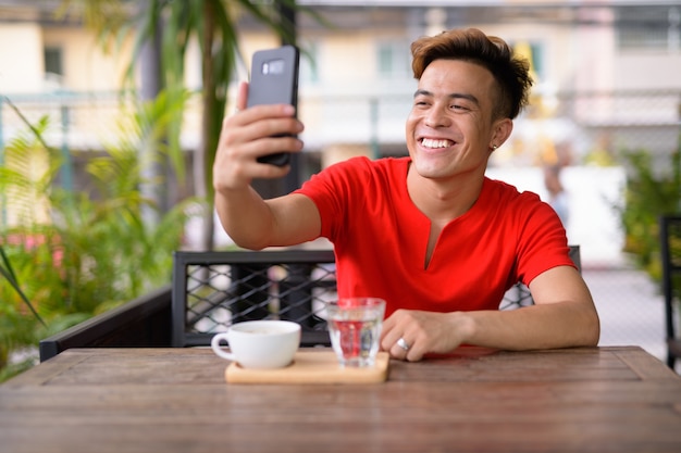 Gelukkig jonge Aziatische man selfie te nemen bij de coffeeshop buitenshuis