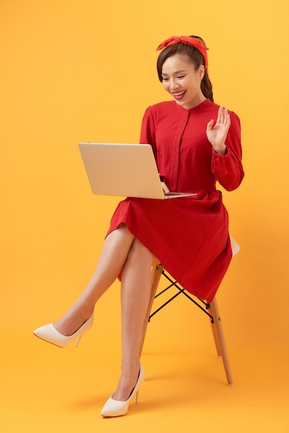 Gelukkig jonge Aziatische vrouw met behulp van laptop in fauteuil over oranje achtergrond