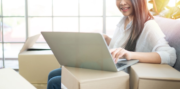 Gelukkig jonge Aziatische vrouw ondernemer, glimlach voor verkoopsucces na het controleren van bestelling van online winkelen winkel in laptop thuis kantoor