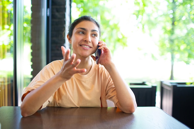 Gelukkig jonge Indiase vrouw praten op mobiele telefoon zitten buitencafé