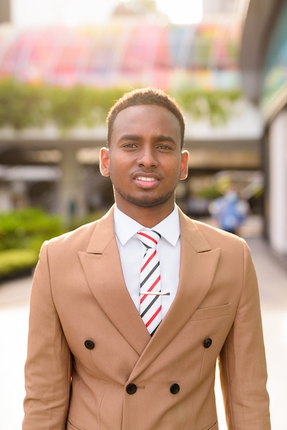 Gelukkig jonge knappe Afrikaanse zakenman glimlachend in de stad met natuur buiten