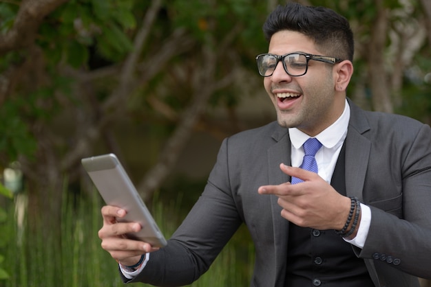 Gelukkig jonge knappe Indiase zakenman videobellen met digitale tablet in het park