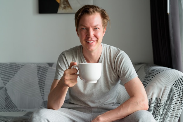 Gelukkig jonge knappe man koffie drinken in de huiskamer