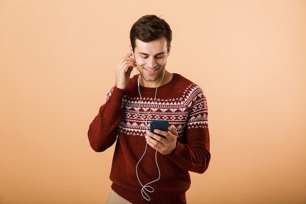 Gelukkig jonge man geïsoleerd over beige muur luisteren muziek chatten via de telefoon