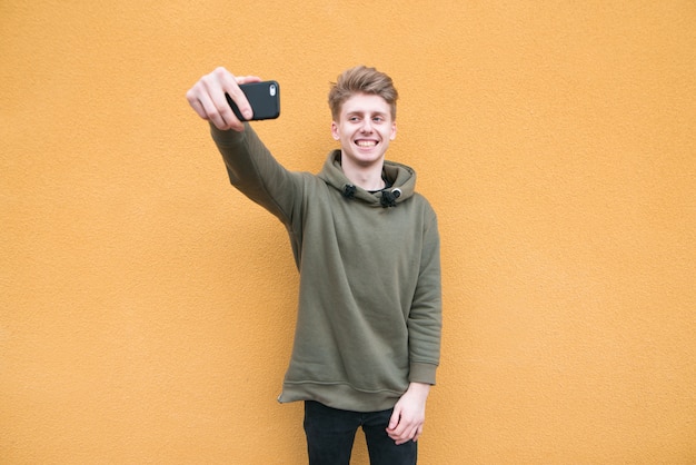 Gelukkig jonge man in casual kleding neemt selfie op een oranje muur.