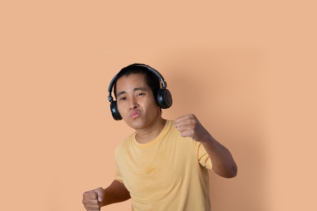 Gelukkig jonge man in koptelefoon luisteren naar muziek en dansen op oranje studio achtergrond. Muziek luisteren.