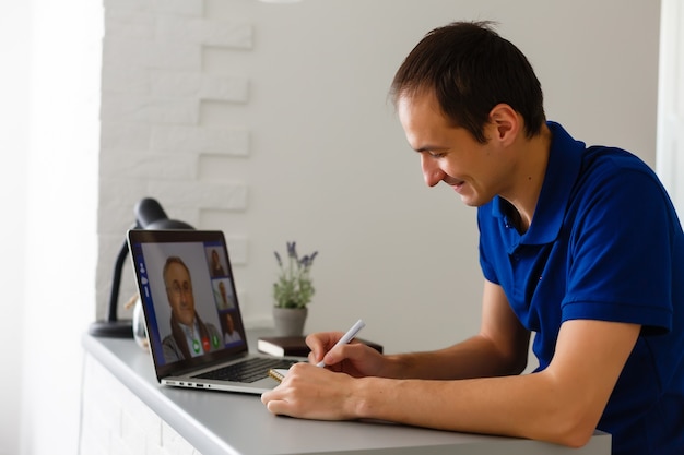 Gelukkig jonge man in t-shirt om thuis te zitten, werken op laptopcomputer, glimlachend.