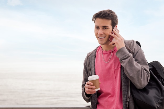 Gelukkig jonge man met een kopje koffie praten via de telefoon