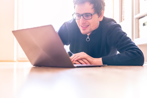 Gelukkig jonge man met een moderne laptop zit op de houten vloer