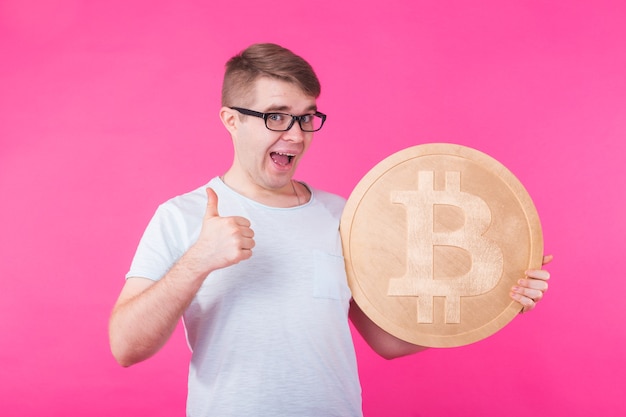 Gelukkig jonge man met grote gouden bitcoin op roze achtergrond