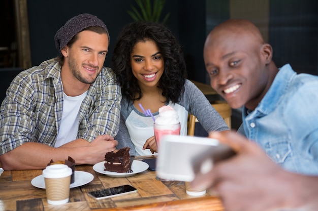 Gelukkig jonge man met vrienden selfie te nemen aan houten tafel in de coffeeshop