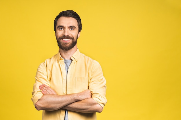 Gelukkig jonge man. Portret van knappe jonge, bebaarde man in casual glimlach terwijl geïsoleerd over gele achtergrond.