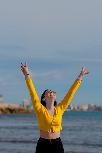 Foto gelukkig jonge man steekt zijn handen vreugdevol aan de oever van het strand met de blauwe zee-achtergrond