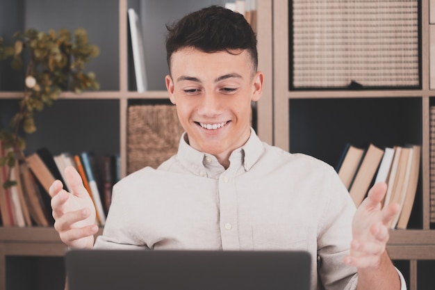 Gelukkig jonge man tiener glimlachend en praten in videoconferentie studeren en online leren met school. Millennial huiswerk maken thuis bellen