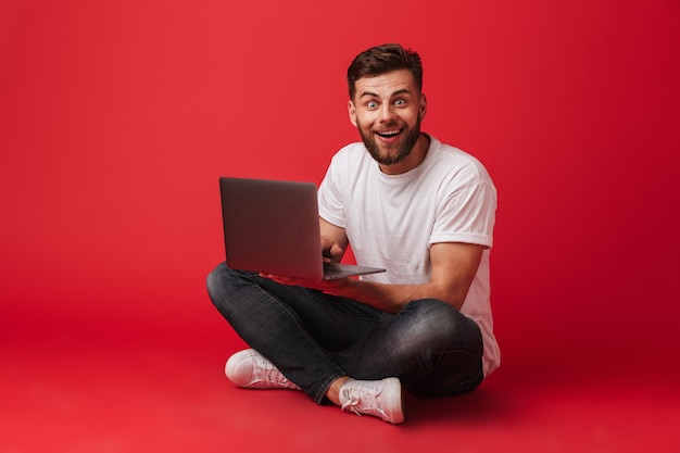 Gelukkig jonge man zit geïsoleerd met behulp van laptop computer.